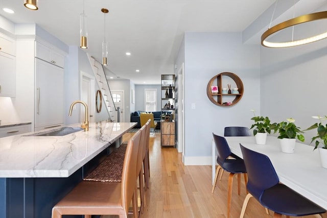 424-430 W 4th St Unit 428, Boston, MA 02127 - kitchen featuring light wood-style floors, light stone countertops, white cabinets, hanging light fixtures, and a kitchen island with sink