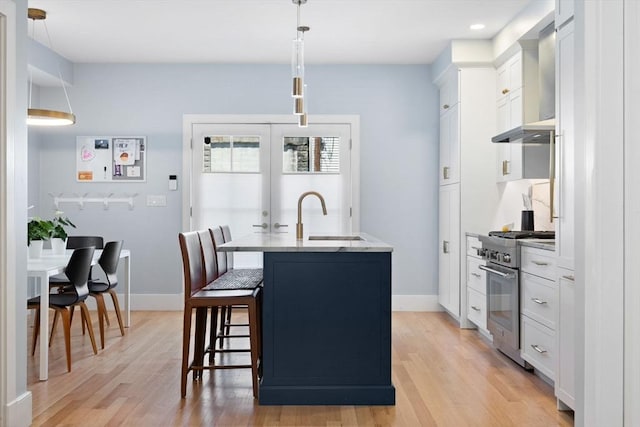 424-430 W 4th St Unit 428, Boston, MA 02127 - kitchen featuring stainless steel stove, wall chimney range hood, light wood finished floors, a kitchen breakfast bar, and white cabinets