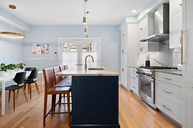 424-430 W 4th St Unit 428, Boston, MA 02127 - kitchen with wall chimney exhaust hood, stainless steel stove, light wood-style flooring, an island with sink, and white cabinetry
