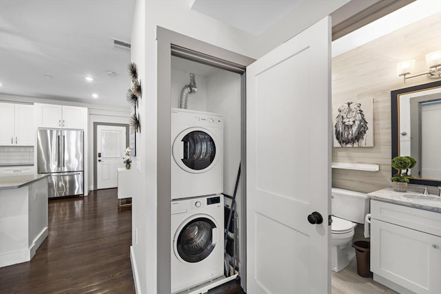 laundry area featuring sink, stacked washer / dryer, and dark hardwood / wood-style floors