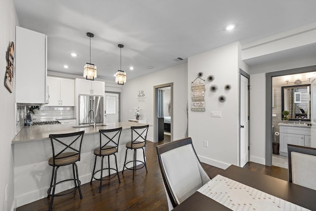 kitchen featuring a breakfast bar area, hanging light fixtures, high end refrigerator, white cabinetry, and tasteful backsplash