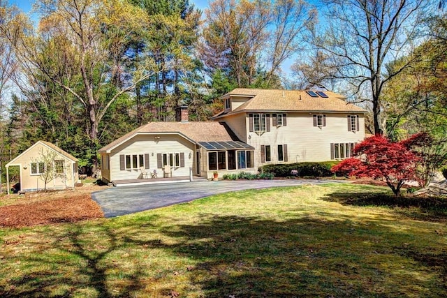 back of house featuring a lawn, a chimney, an outdoor structure, and aphalt driveway