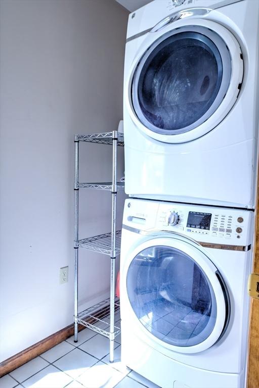 clothes washing area featuring light tile patterned floors, laundry area, and stacked washer / dryer