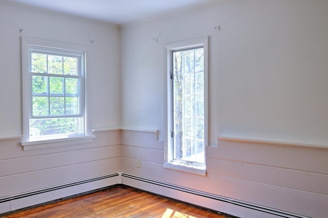 spare room featuring plenty of natural light, a baseboard heating unit, and wood finished floors