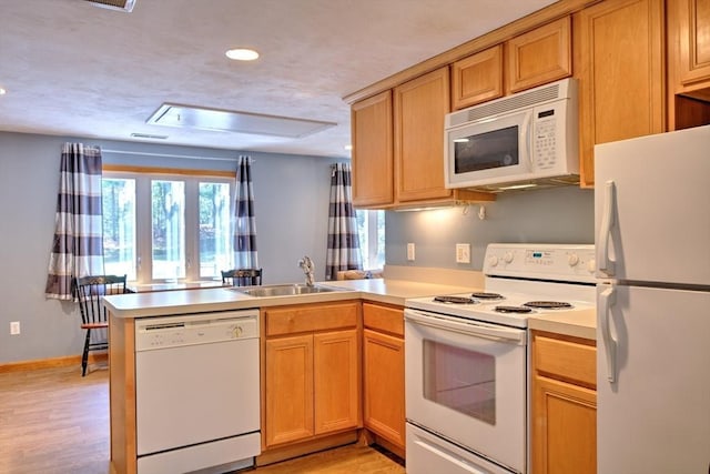 kitchen with a peninsula, white appliances, light wood-type flooring, light countertops, and a sink