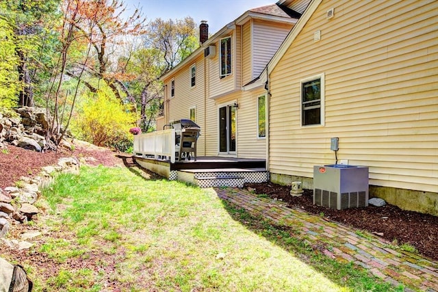 rear view of house with an AC wall unit, a wooden deck, a chimney, and a yard