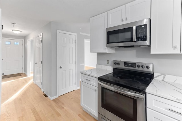 kitchen with stainless steel appliances, light stone countertops, white cabinets, and light hardwood / wood-style floors