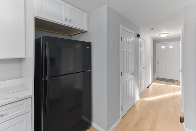 kitchen with light stone countertops, black refrigerator, white cabinets, and light hardwood / wood-style flooring