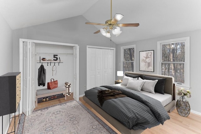 bedroom featuring lofted ceiling, ceiling fan, wood-type flooring, and multiple closets