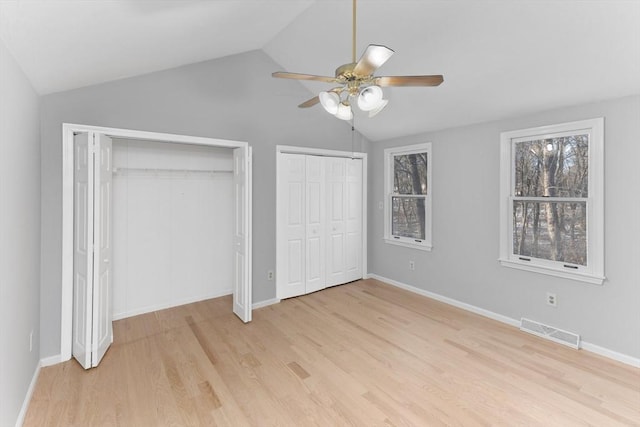 unfurnished bedroom featuring ceiling fan, lofted ceiling, light wood-type flooring, and two closets