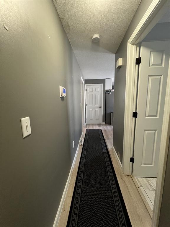 hallway with a textured ceiling and light wood-type flooring