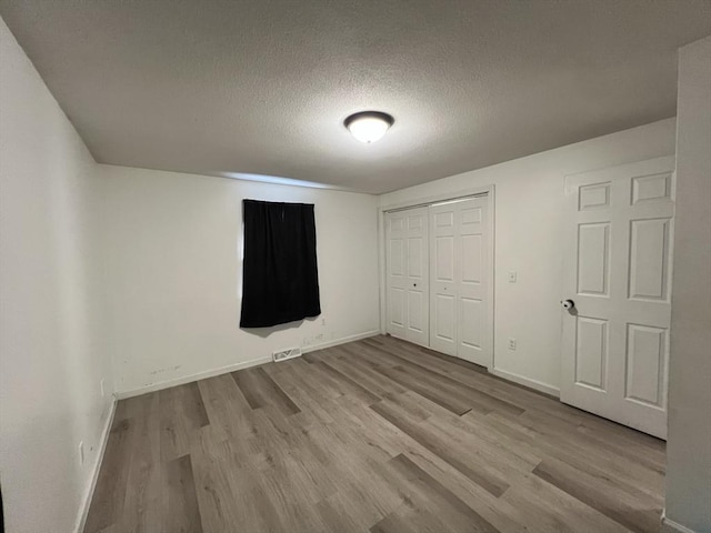 unfurnished bedroom featuring a textured ceiling, light wood-type flooring, and a closet