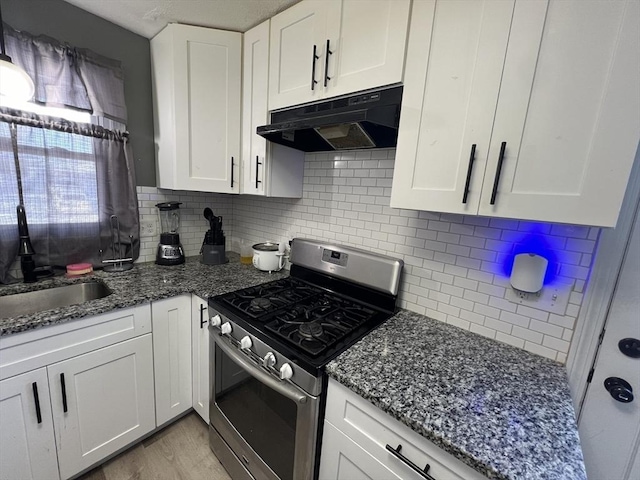 kitchen featuring sink, dark stone countertops, white cabinets, backsplash, and gas range