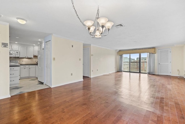 unfurnished living room featuring a chandelier, baseboards, and visible vents