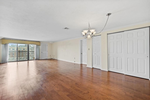 unfurnished living room featuring wood finished floors, ornamental molding, baseboards, visible vents, and a notable chandelier
