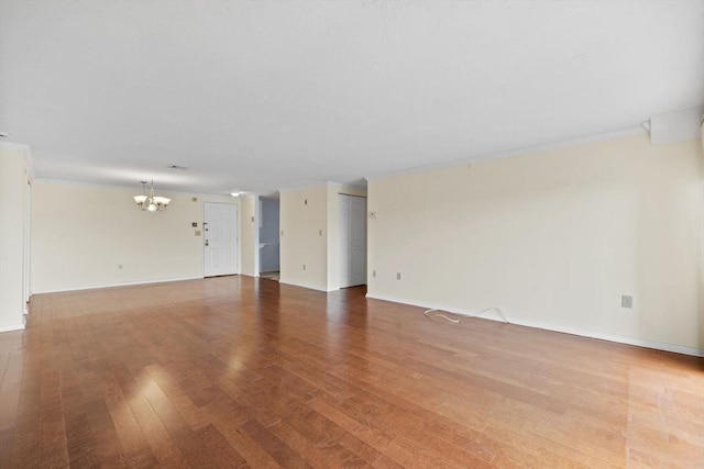empty room featuring baseboards, a chandelier, and wood finished floors
