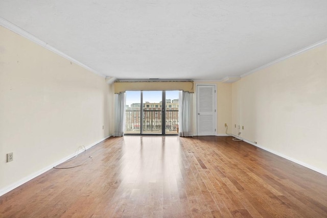 empty room with crown molding, light wood-style flooring, and baseboards
