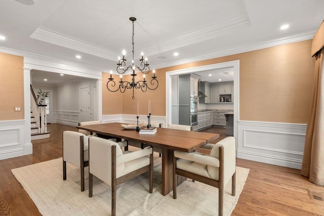 dining space featuring a raised ceiling, wainscoting, and light wood-style flooring