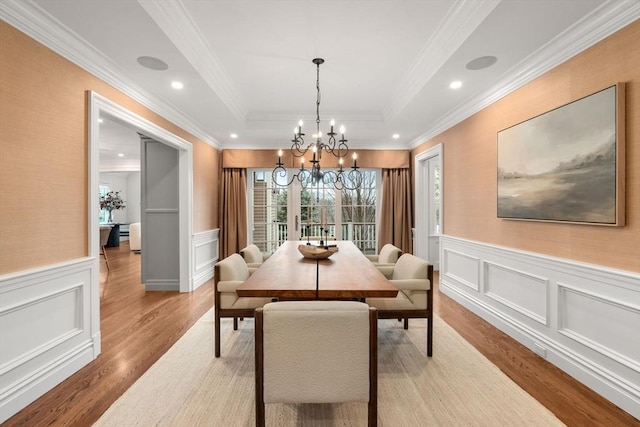 dining area with a wainscoted wall, recessed lighting, a raised ceiling, a chandelier, and light wood-type flooring