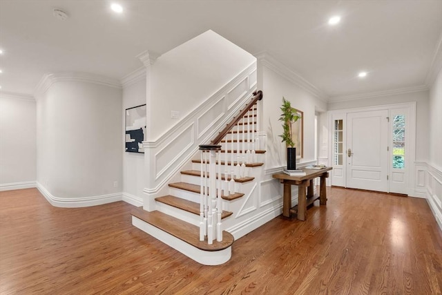 entrance foyer featuring crown molding, a decorative wall, stairway, and wood finished floors