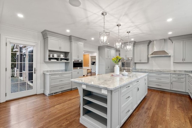 kitchen featuring dark wood-style flooring, a center island with sink, open shelves, gray cabinets, and wall chimney exhaust hood