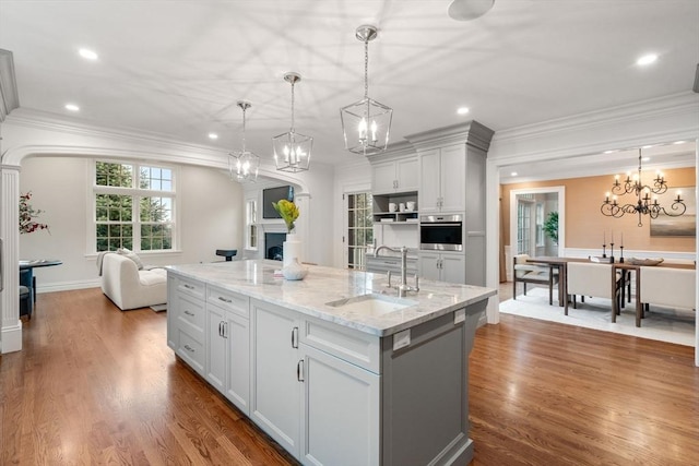 kitchen with a notable chandelier, a fireplace, a sink, stainless steel oven, and a center island with sink