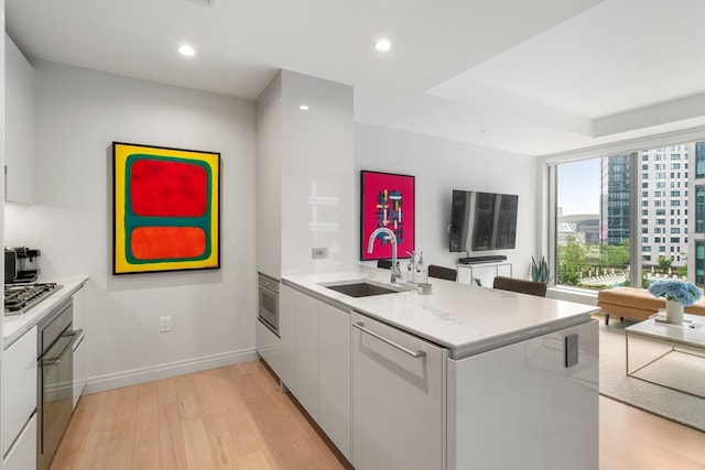 kitchen with wall oven, dishwasher, kitchen peninsula, sink, and light wood-type flooring