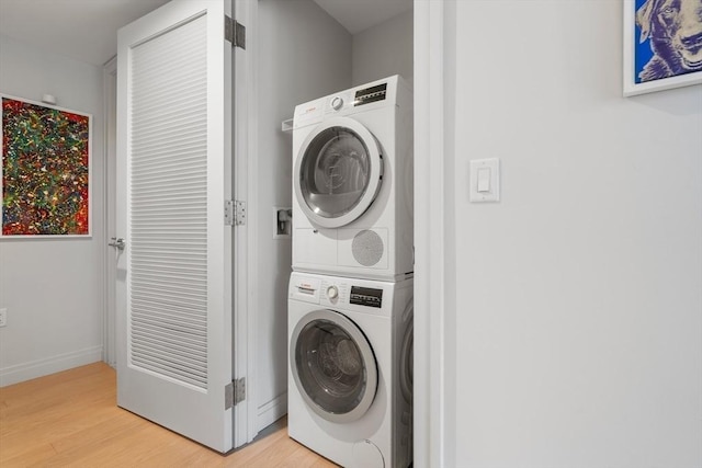 clothes washing area featuring laundry area, stacked washer and dryer, light wood-style floors, and baseboards