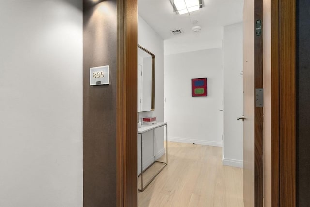 hall with visible vents, light wood-style flooring, and baseboards