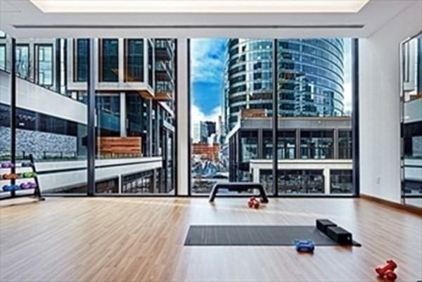 gym with a city view, wood finished floors, floor to ceiling windows, and a healthy amount of sunlight