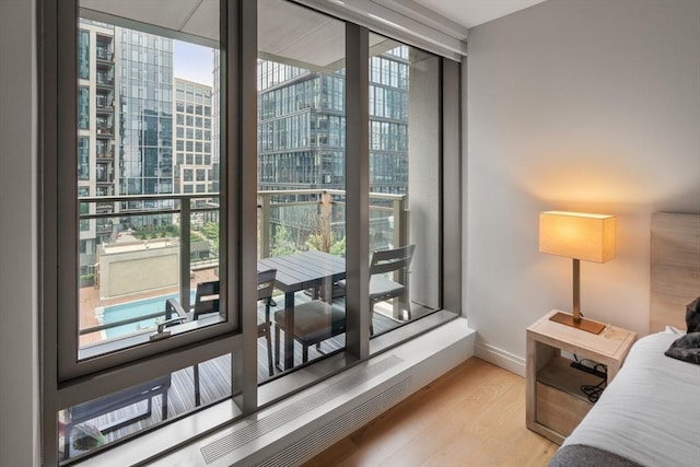 bedroom featuring a wall of windows, a view of city, baseboards, and light wood-type flooring