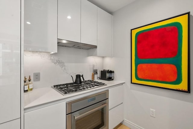 kitchen with backsplash, under cabinet range hood, light countertops, white cabinets, and stainless steel appliances