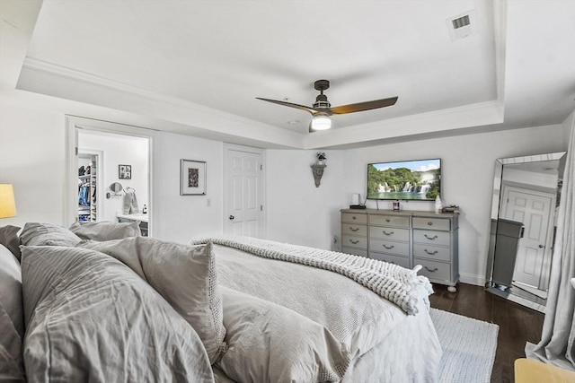 bedroom with ceiling fan, dark hardwood / wood-style flooring, connected bathroom, and a tray ceiling