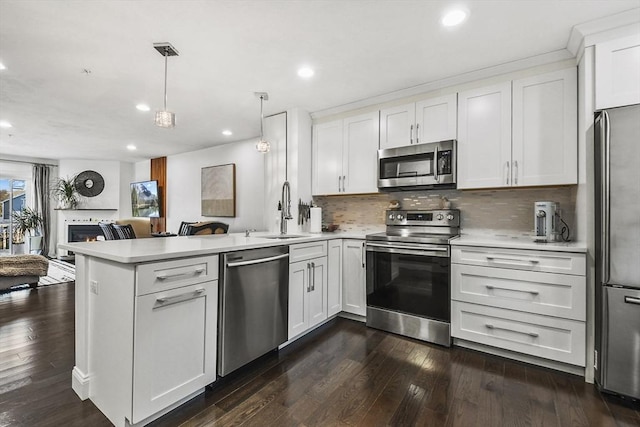 kitchen featuring stainless steel appliances, hanging light fixtures, kitchen peninsula, sink, and white cabinetry