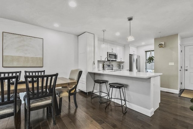 kitchen with white cabinets, kitchen peninsula, a breakfast bar area, hanging light fixtures, and appliances with stainless steel finishes