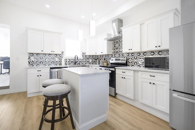 kitchen with stainless steel appliances, wall chimney range hood, a kitchen island, light wood finished floors, and recessed lighting