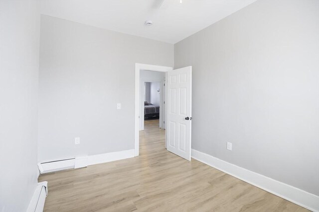empty room featuring baseboard heating, light wood-style flooring, and baseboards