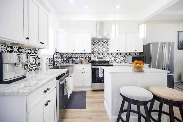 kitchen featuring appliances with stainless steel finishes, wall chimney exhaust hood, a sink, a kitchen breakfast bar, and light wood-style flooring