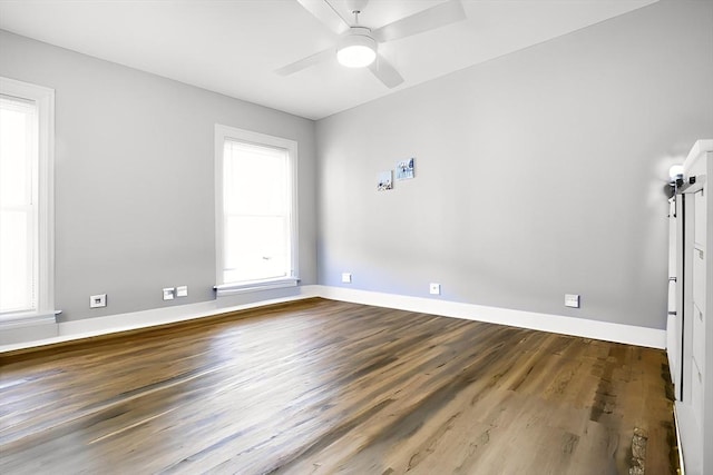 unfurnished room featuring healthy amount of natural light, dark wood-style floors, a ceiling fan, and baseboards