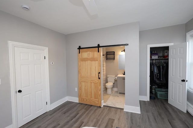 unfurnished bedroom with a barn door, dark wood-type flooring, a closet, baseboards, and ensuite bathroom
