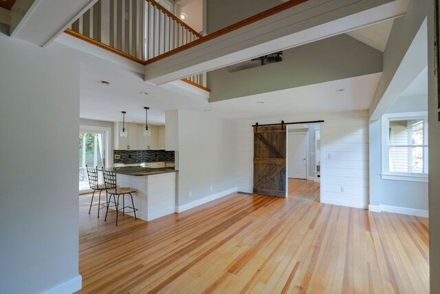 unfurnished living room featuring a barn door, a towering ceiling, and light wood-type flooring