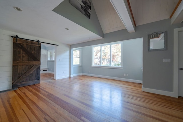 unfurnished living room featuring beam ceiling, light hardwood / wood-style flooring, a barn door, and wooden walls