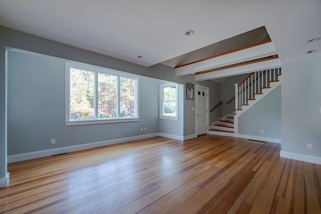 unfurnished living room featuring beam ceiling and light hardwood / wood-style floors