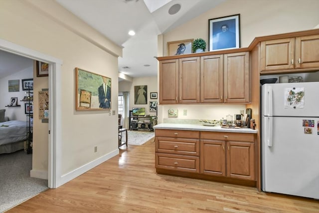 kitchen featuring vaulted ceiling with skylight, light wood-style floors, light countertops, and freestanding refrigerator
