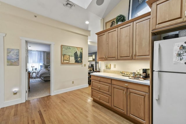 kitchen featuring vaulted ceiling, light countertops, freestanding refrigerator, visible vents, and light wood-style floors