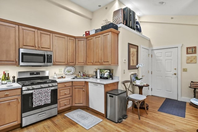 kitchen featuring light countertops, a sink, brown cabinets, light wood-style flooring, and stainless steel appliances