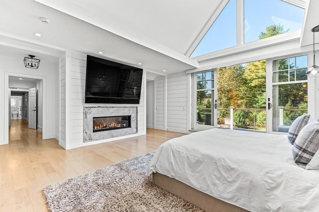 bedroom featuring multiple windows, a premium fireplace, high vaulted ceiling, and light wood-type flooring