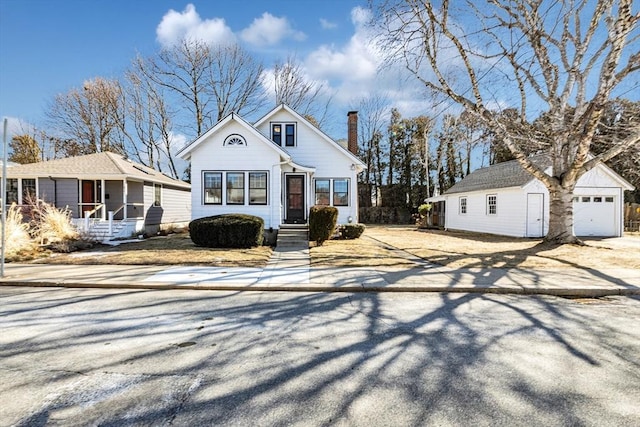 bungalow-style home featuring a garage, a chimney, a porch, and an outbuilding