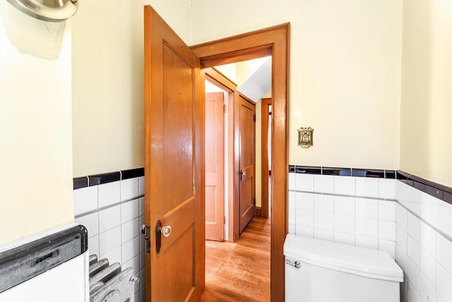 half bathroom with wainscoting, tile walls, toilet, and wood finished floors