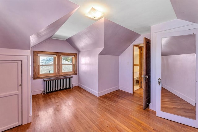 additional living space featuring lofted ceiling, light wood-style floors, baseboards, and radiator